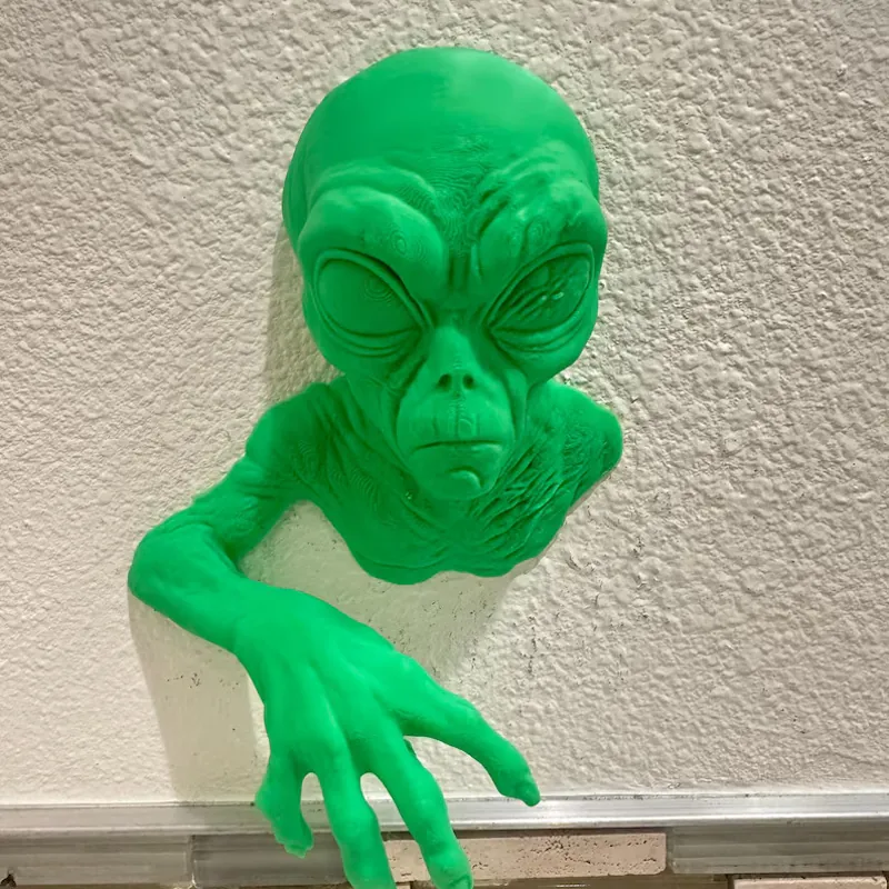Green 3D printed alien climbing out of a wall