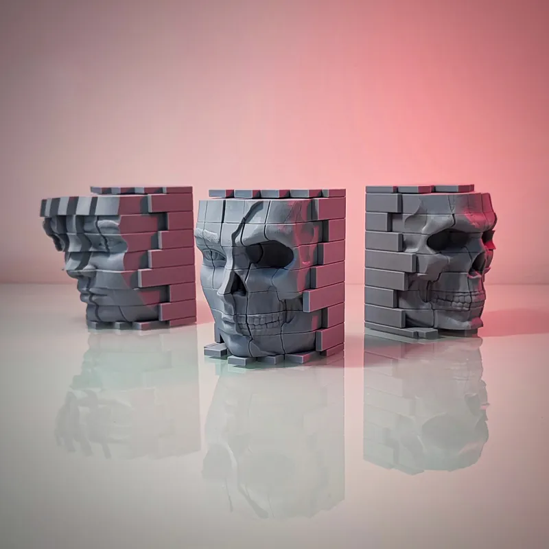 Three grey 3D printed pixel skull planters on a reflective surface