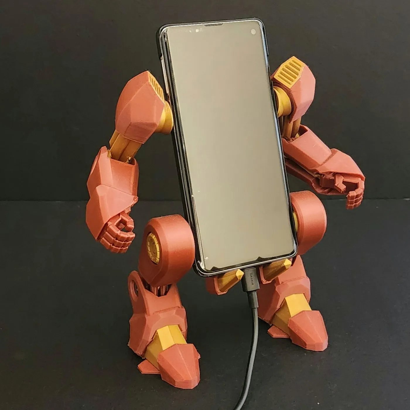 3D printed red and gold robot exo-suit holding a charging smartphone