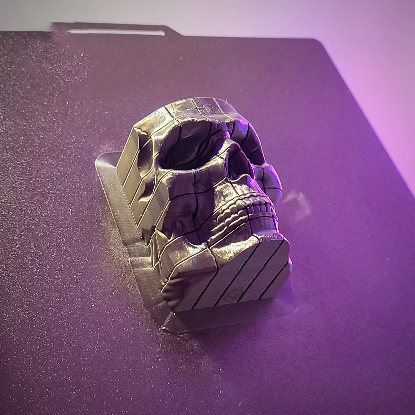 Dark 3D printed pixel skull on a textured print bed under purple light