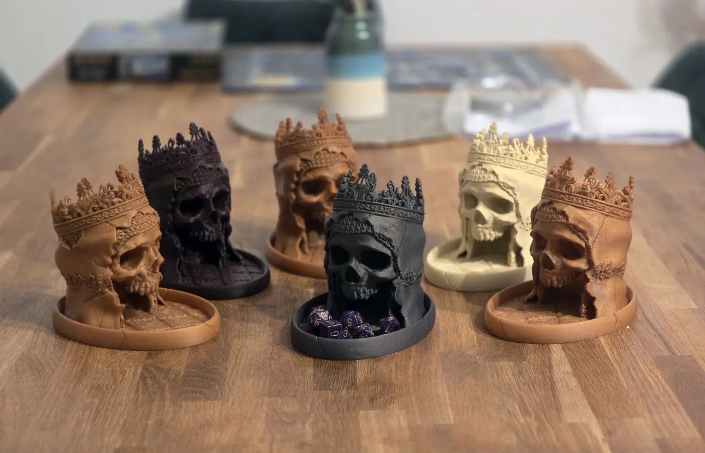Six 3D printed crowned skull dice towers in bronze, black and bone colours on a table